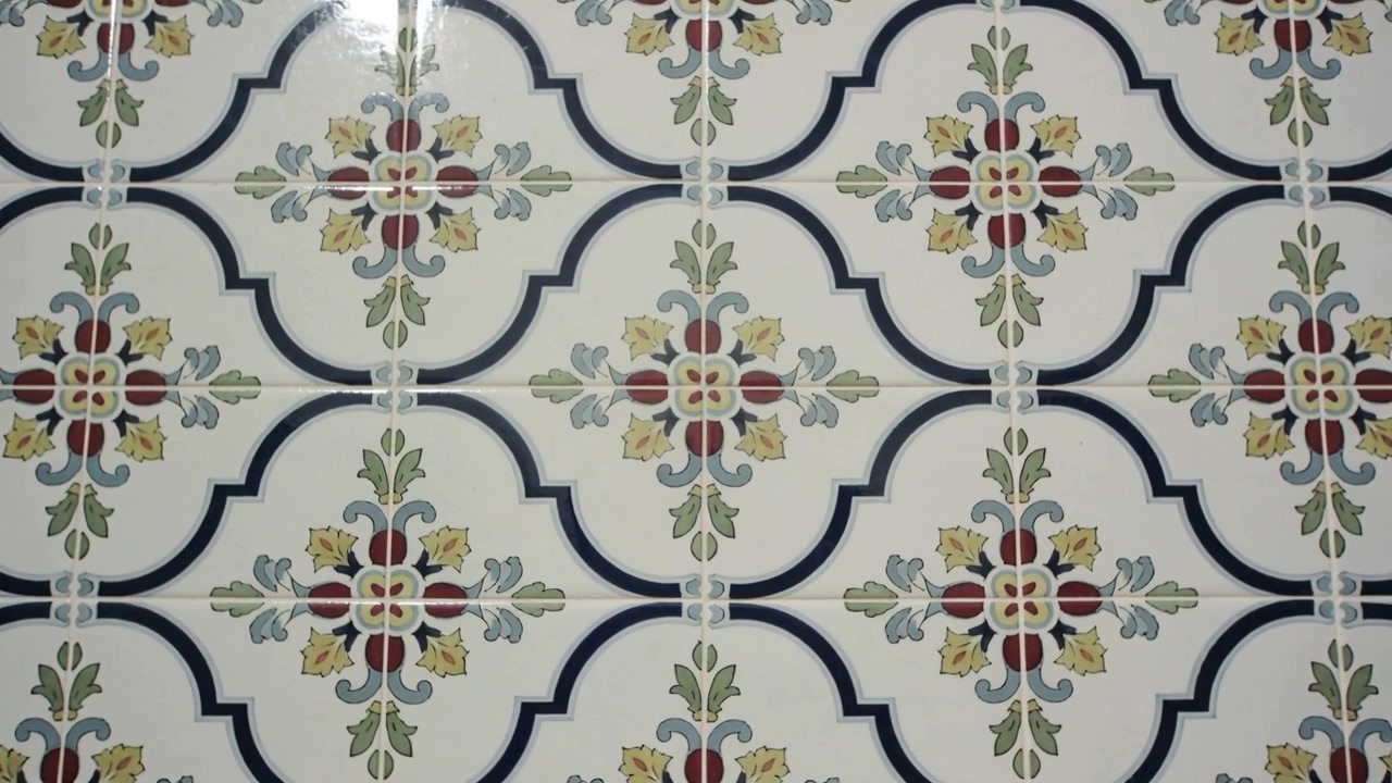 Câmera com zoom estudando azulejos esmaltados na parede da cozinha, mostrando um quadrifólio azul-marinho e medalhões florais.