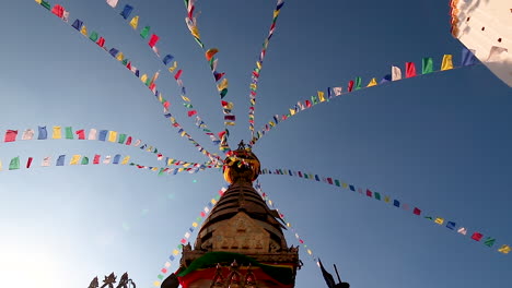 low angle wide shot of famous swayambhunath stupa pinnacle against the blue sky. slow motion of prayer flags.