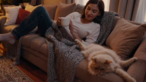 woman relaxing on a couch with her cat and a mug in a cozy living room