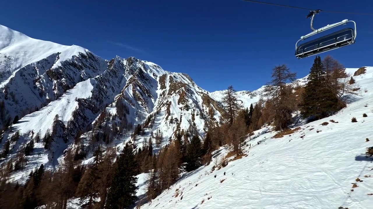 Una seggiovia scivola su pendii innevati in una regione alpina, incorniciata da montagne aspre e cieli azzurri e limpidi. Ideale per sport invernali o progetti a tema viaggio