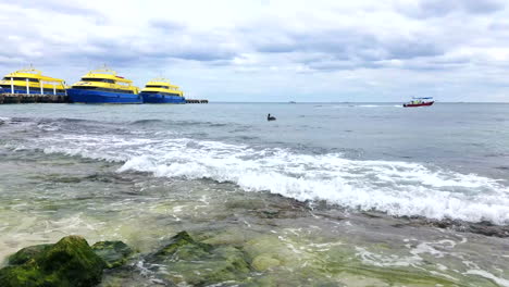 Boat-Driving-Off-And-Pelican-Floating-In-The-Water-With-Cruise-Ferry-Ships-And-Pier-On-The-Horizon