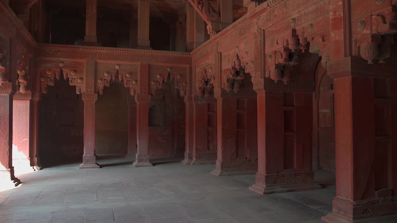 Toma interior amplia y estática de pilares de arenisca roja tallados y arcos ornamentados dentro del Jahangiri Mahal en el Fuerte de Agra, en Uttar Pradesh, India.