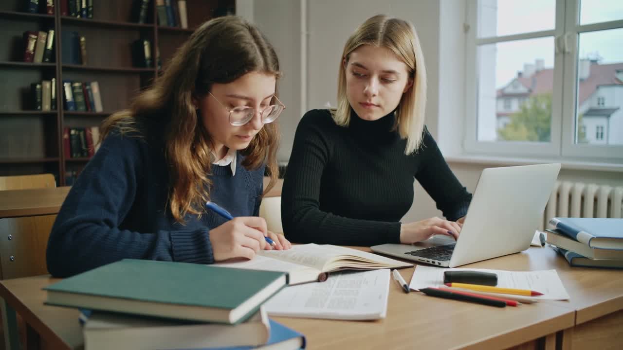 Vertikal video: To studenter studerer, den ene blar og noterer i en bok til venstre, den andre skriver digitale notater på en bærbar datamaskin til høyre