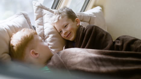 two little brothers talking and laughing together while lying under a blanket in the campervan bed