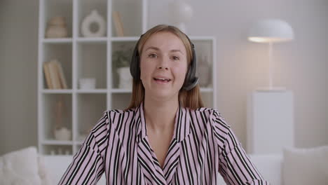 young friendly woman is speaking looking at camera communicating online using headphones with microphone