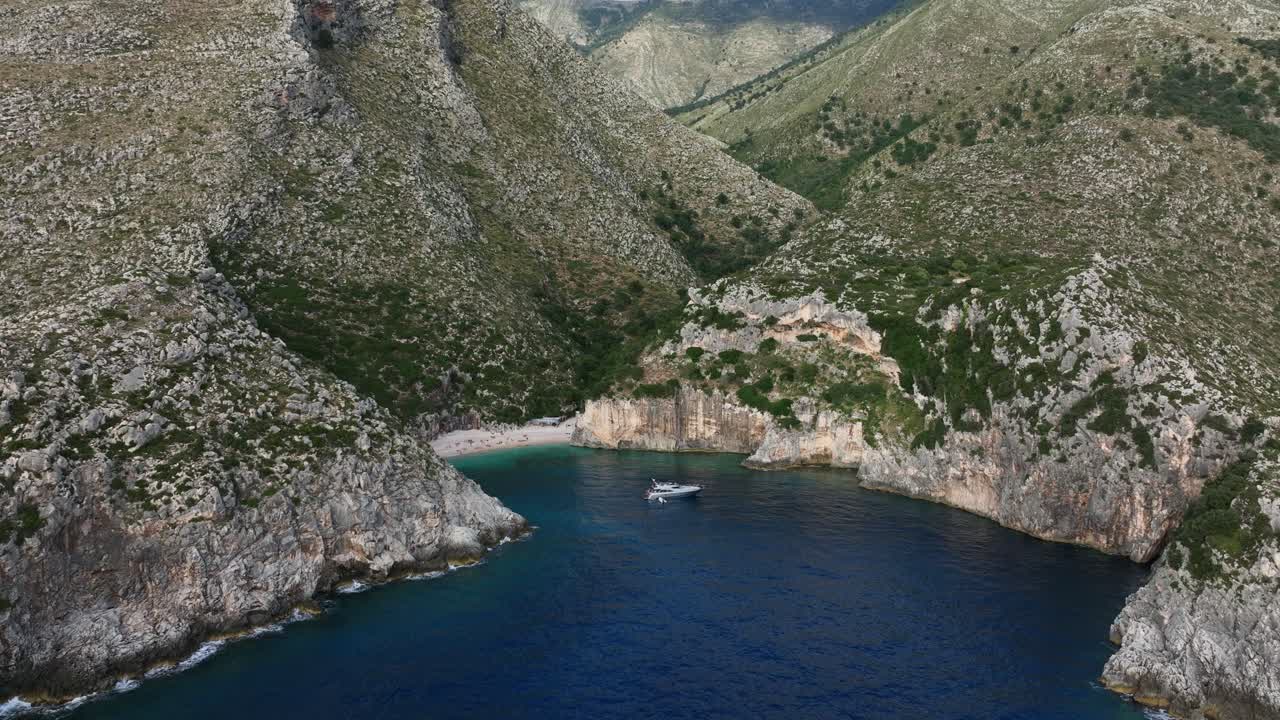 Yacht anchored in rocky inlet and rugged hills near ocean water at Shpella, Albania, aerial dolly