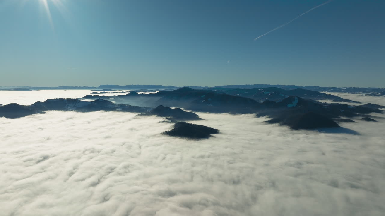 Vue sur les Alpes slovènes s’élevant au-dessus d’une couche de nuages. La vidéo montre des sommets montagneux émergeant de la brume, avec un ciel dégagé au-dessus, créant une atmosphère alpine calme et étendue.