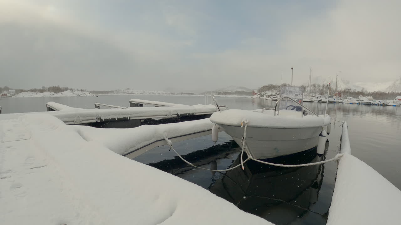 Ripresa panoramica a mano di una barca in un porto turistico pesantemente innevato con leggera nevicata a Ringstad, Vesterålen, Norvegia