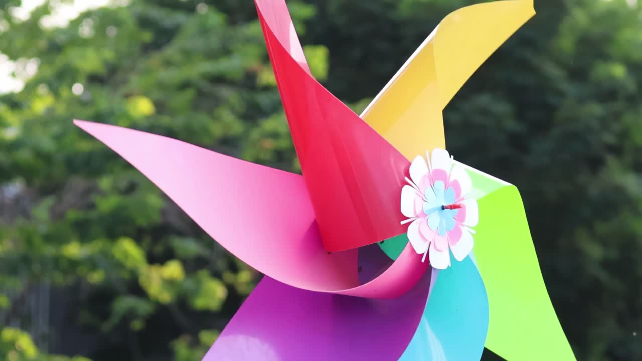 A colorful pinwheel spins energetically against a backdrop of dense green foliage, showcasing dynamic motion and vivid hues.