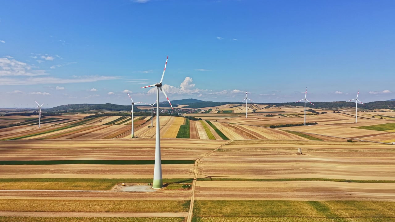 Wind turbines stand tall in farmland under a clear blue sky during daytime with some clouds in the background