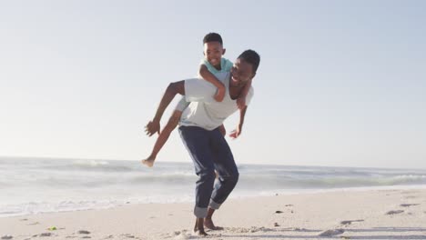 retrato de un padre afroamericano sonriente llevando a su hijo en una playa soleada