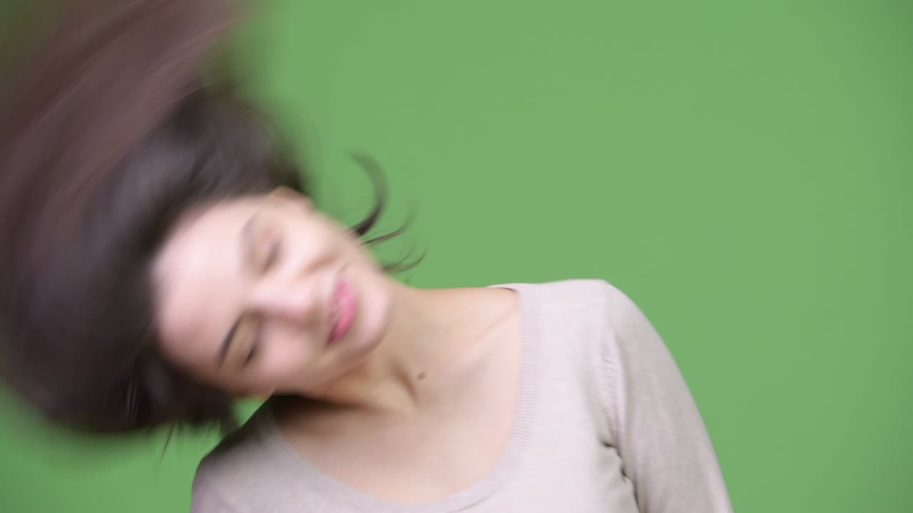 Young beautiful woman flipping hair against green background