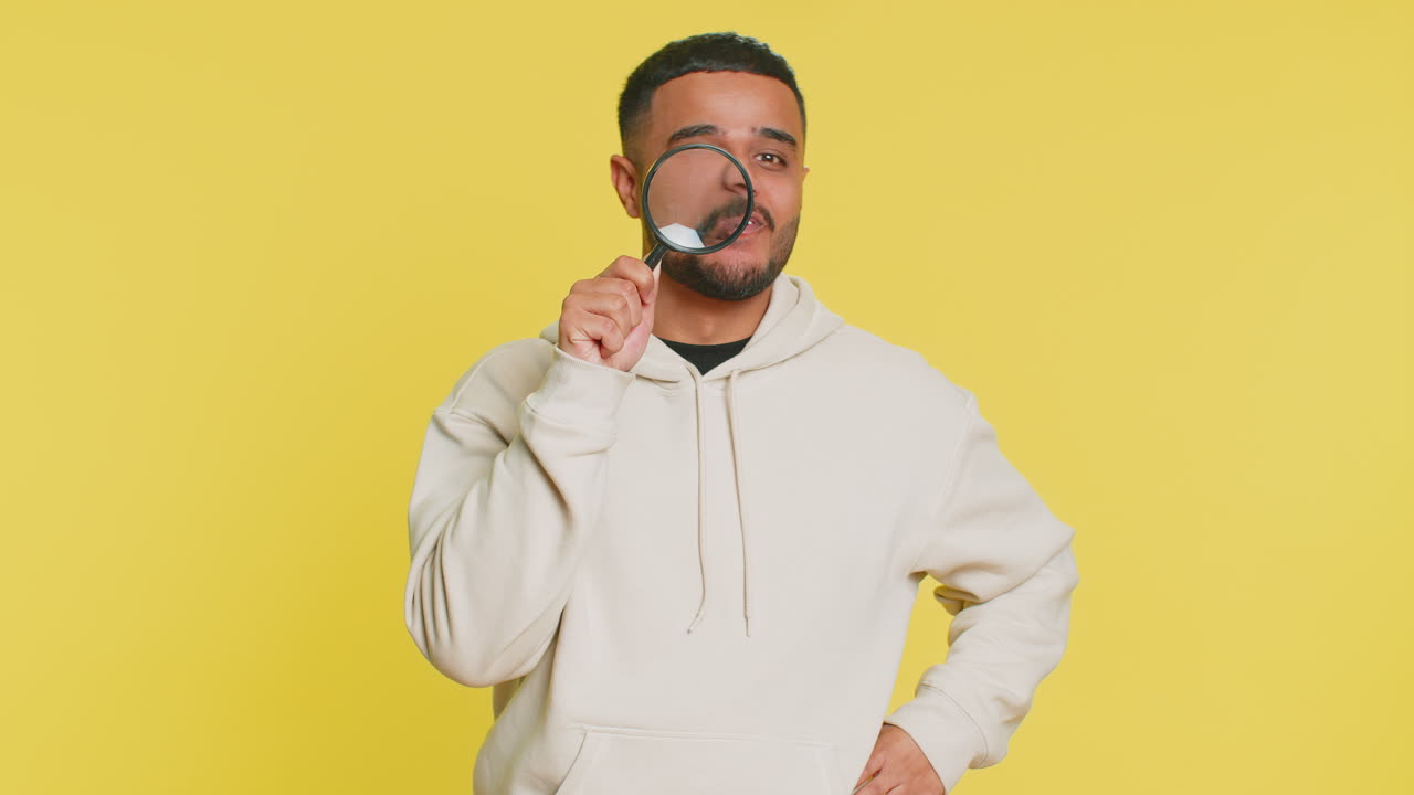 joven indio sostiene una lupa cerca de la cara mirando a la cámara con un gran ojo ampliado analizando