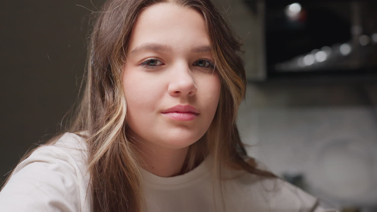 Portrait youngster swiping hands over face making funny faces, playful motion near camera, kitchen background blur, skin, long hair strands, spontaneous gesture in close view with youthful energy