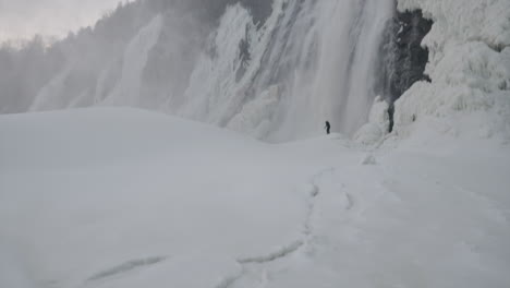 girl standing in thick icy surface near a waterfall in quebec in winter - pan up wide shot