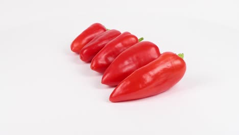 cinco pimientos dulces rojos sobre fondo blanco. los pimientos están clasificados de más pequeños a más grandes. movimiento de bucle. vista lateral. rotación 360.