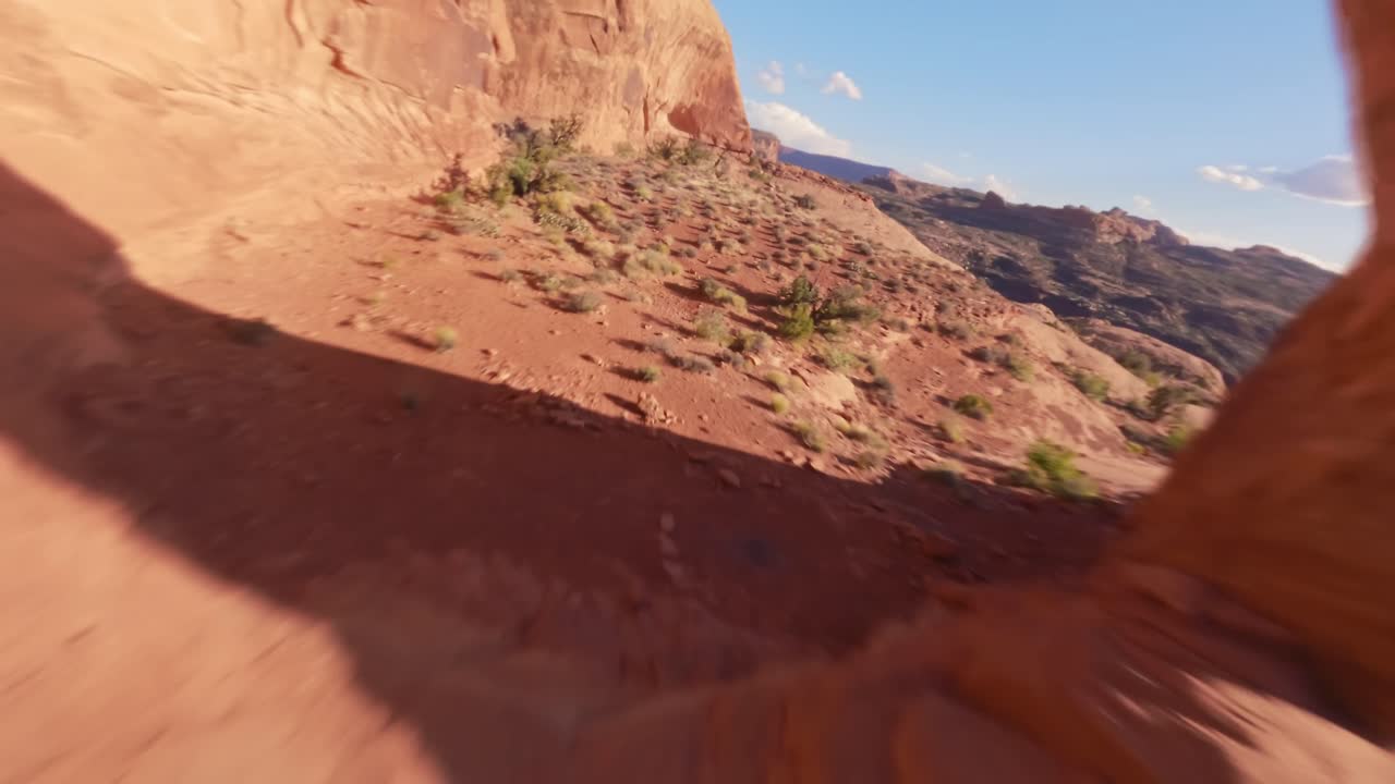 An FPV drone diving and flying through the hidden red sandstone Funnel Arch in the sandy and rocky desert of Moab Utah