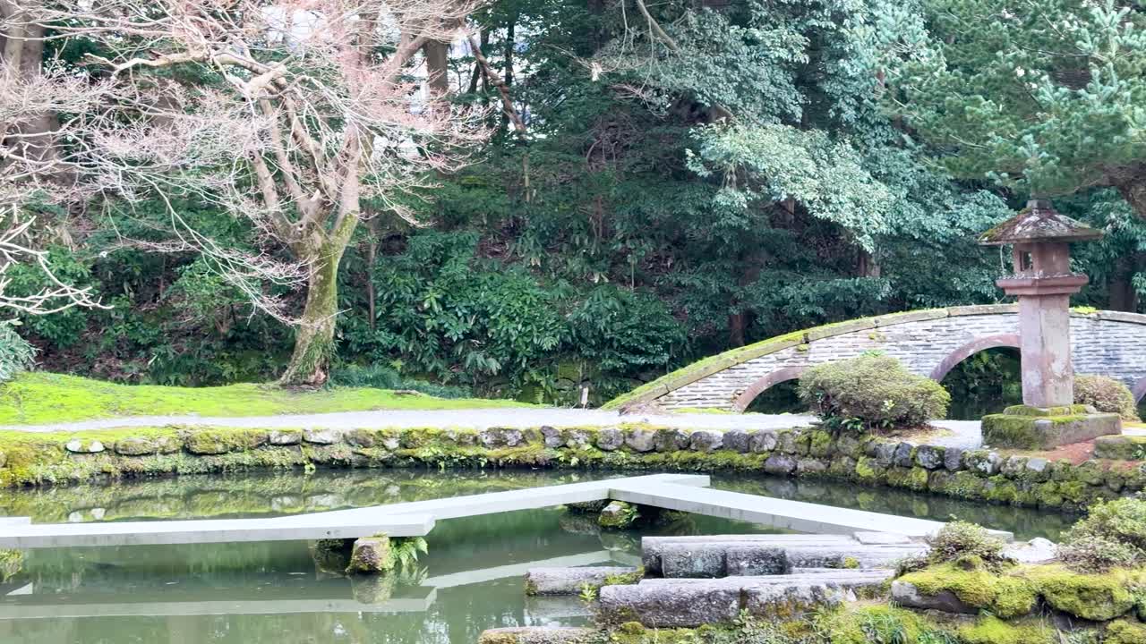 石橋と苔むした風景がある静穏な日本庭園をゆっくりと横切るパン撮影