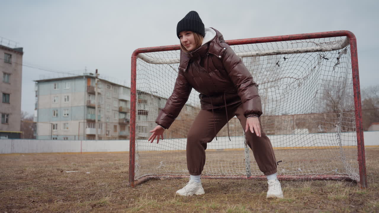 Portero agachado disfrutando de un entrenamiento ligero, portero sonriente practicando ejercicios rápidos de juego de pies, portero relajado con ropa de invierno cómoda participando en ejercicios divertidos cerca de edificios residenciales