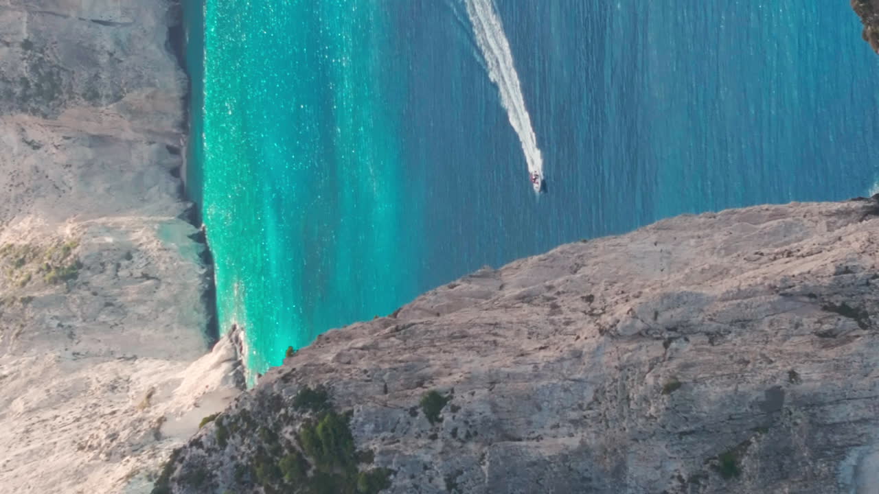 disparo vertical de avión no tripulado, barco a motor navegando en agua de mar turquesa bajo los acantilados de la isla griega de zakynthos
