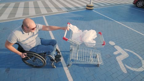 man with disabilities in wheelchair pushing cart in front of himself at supermarket parking