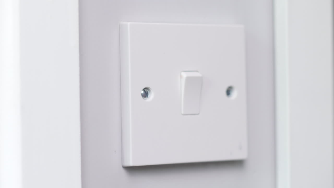 A light switch being turned by a man at night in a dark room