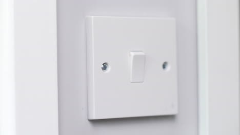 A light switch being turned by a man at night in a dark room