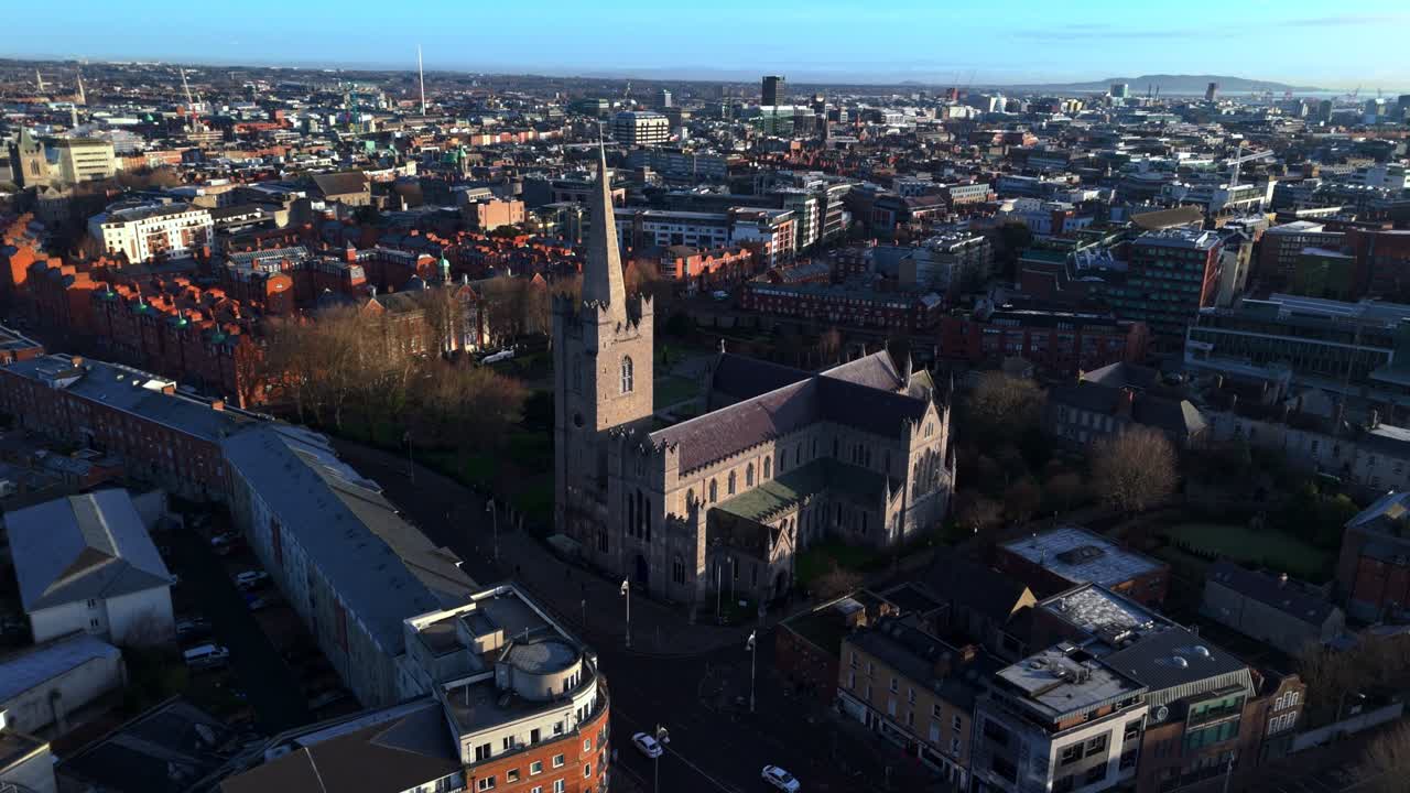 Ripresa aerea con drone della Cattedrale di San Patrizio nella capitale dell'Irlanda, Dublino. Scatto realizzato durante un'alba invernale dorata con vista sul parco, la sua erba e i suoi alberi. Architettura e città irlandese luminosa.