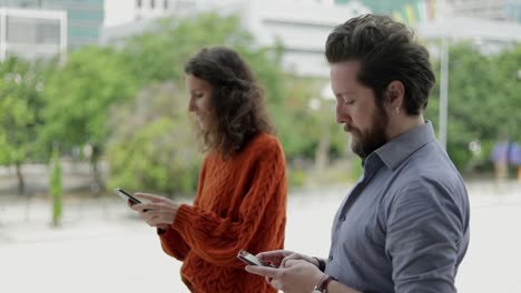 vista lateral de un hombre y una mujer usando teléfonos inteligentes al aire libre