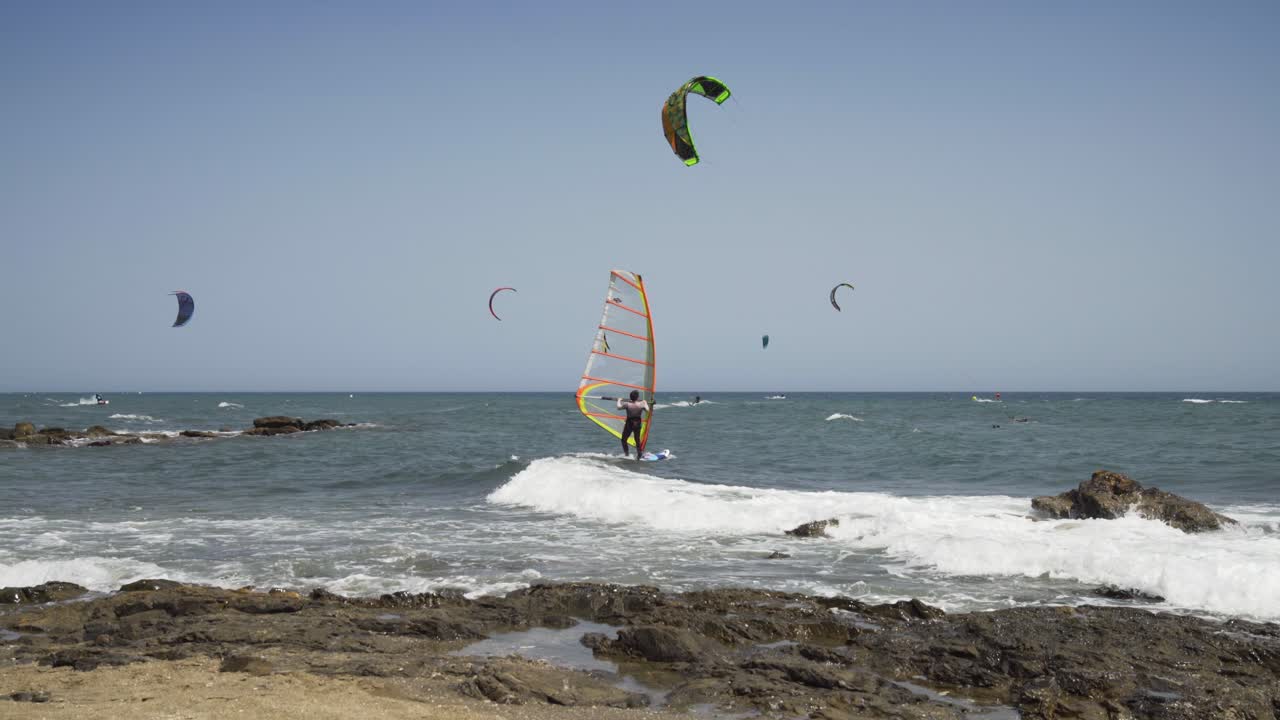 A wind surfer prepares himself in the shallow waters of Cala De Mijas on the Costa Del Sol, steps on to his board and sails off out to sea while kite surfers sail in the background