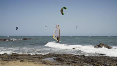 a wind surfer prepares himself in the shallow waters of cala de mijas on the costa del sol, steps on to his board and sails off out to sea while kite surfers sail in the background