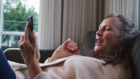 Happy-senior-caucasian-woman-relaxing-and-making-video-call-using-smartphone,-talking-and-smiling