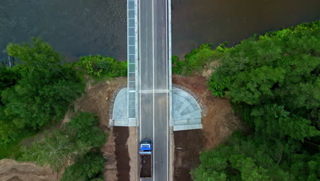 aerial drone top down shot over a truck moving over a bridge surrounded by green vegetation on a cloudy day