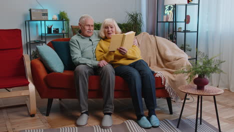 elderly couple reading a book together on the couch