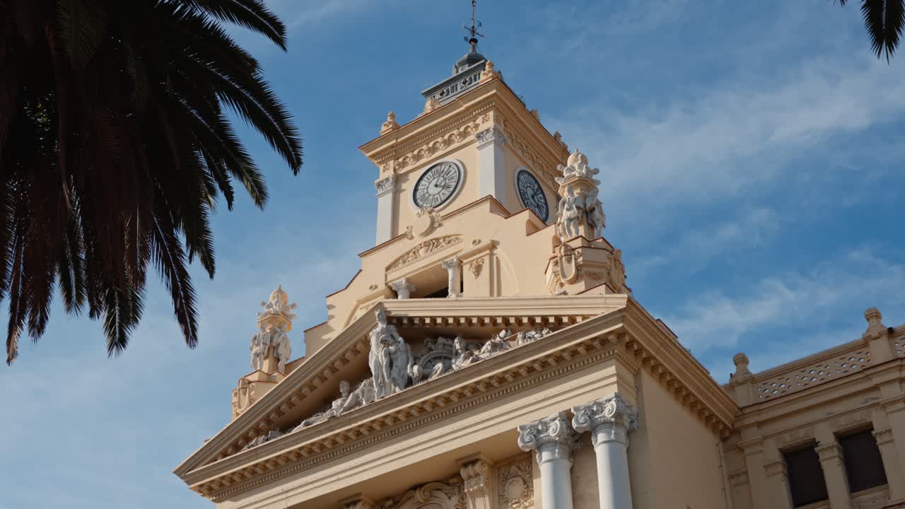 Upward shot of Málaga City Hall, Costa del Sol, Spain, clock tower framed by a tall palm tree against a clear blue sky, capturing elegant Spanish architecture and bright Mediterranean sunlight