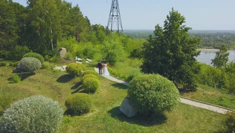 Frischvermähltes-Paar-Spaziert-Entlang-Der-Straße-Im-Grünen-Park-Aus-Der-Vogelperspektive