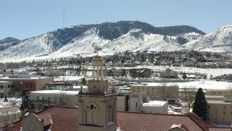 una toma aérea que se mueve hacia atrás y revela una pequeña torre en medio de un pequeño pueblo con vistas a las montañas nevadas