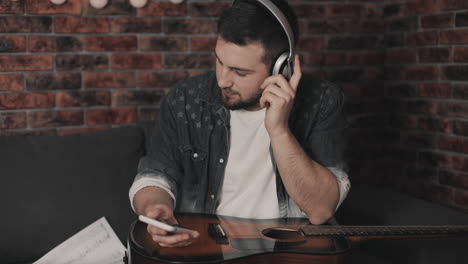 young musician man listening to music with smartphone and wireless headphones at home