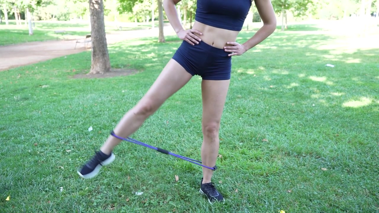 Una donna si allena all'aperto con fasce elastiche, concentrandosi sul miglioramento della sua forma fisica.