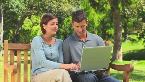 una joven pareja navegando en su computadora portátil en el parque