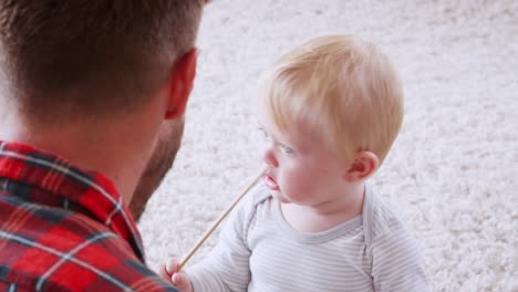 dad playing ukulele to toddler son, over shoulder close up