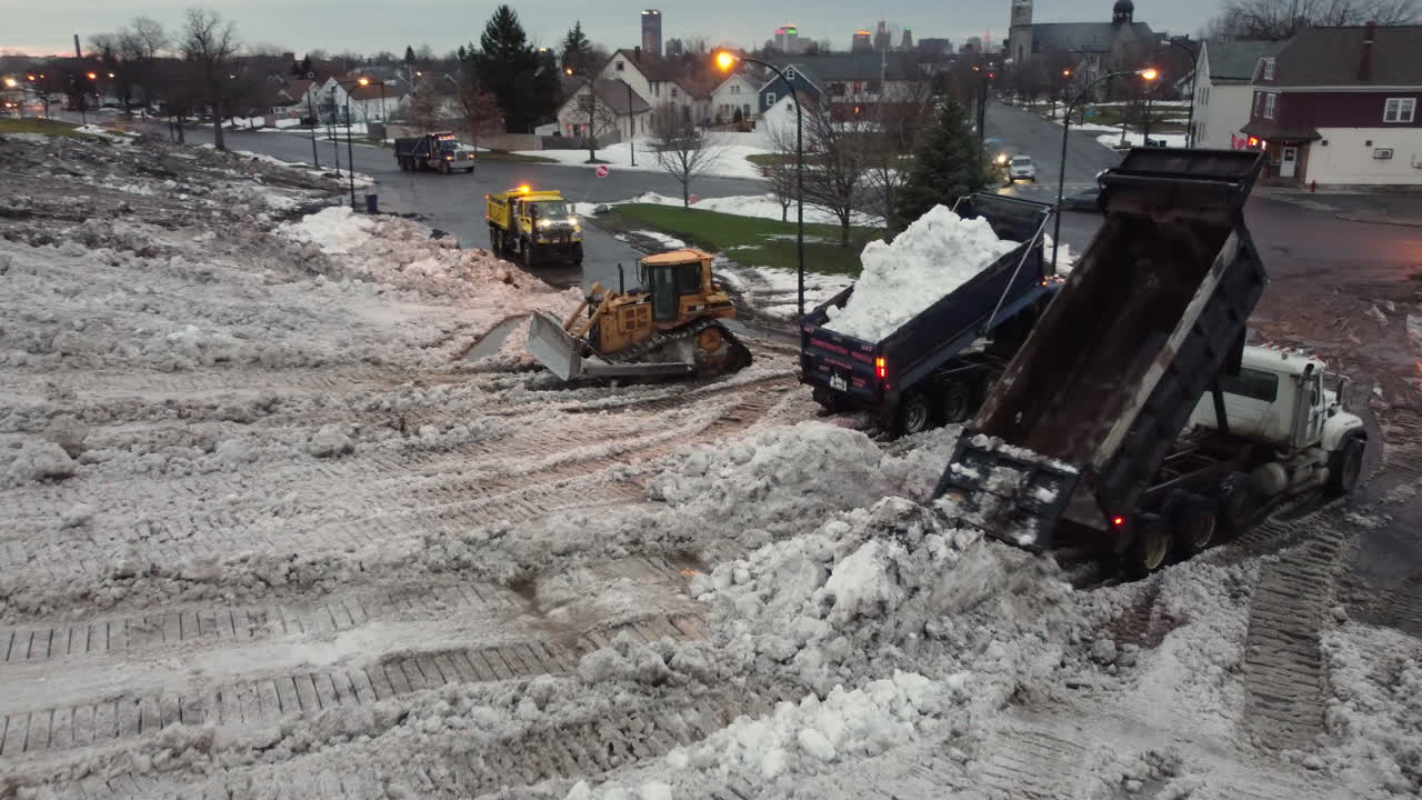 Camion ribaltabili scaricano neve e bulldozer la stanno spostando.
