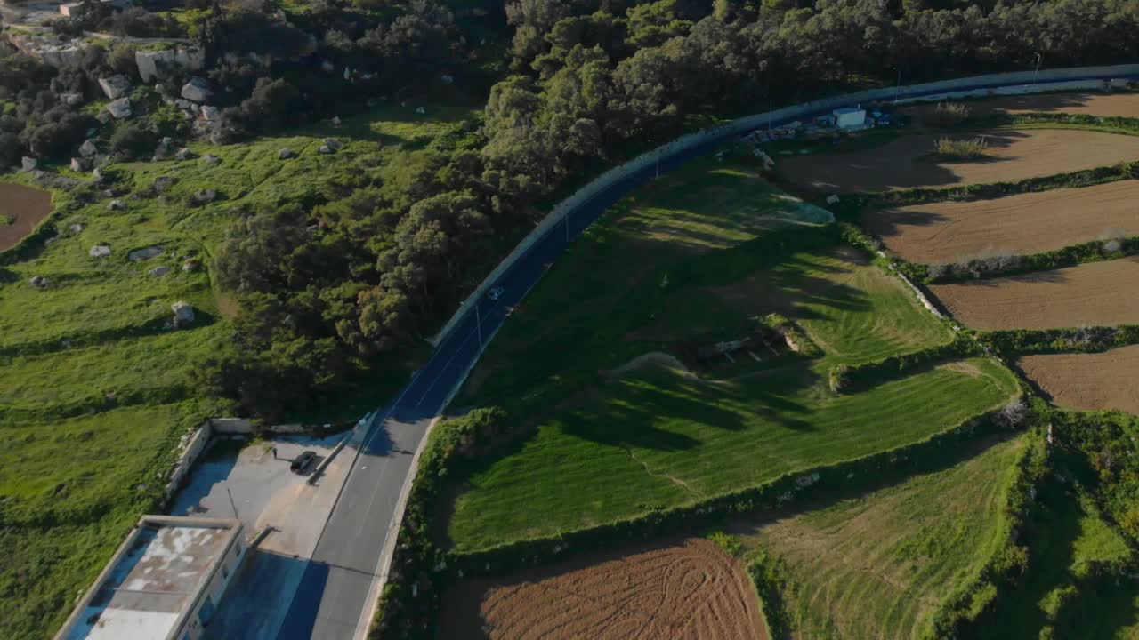Aerial shot of a car driving in a rural area up a hill