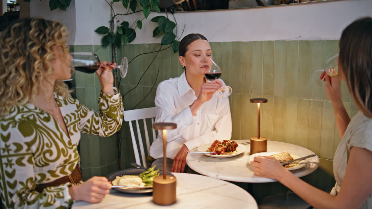 Three female friends toasting with wine at cheerful restaurant dinner closeup