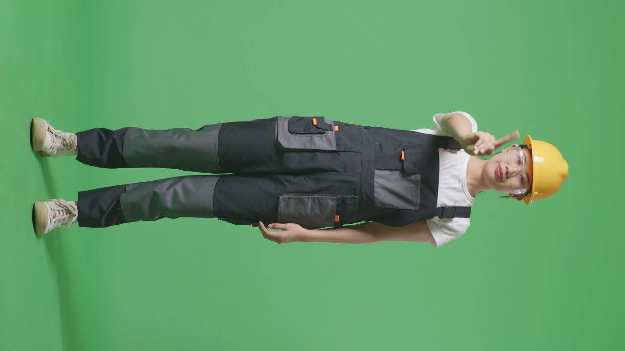 cuerpo lleno de mujer asiática trabajadora con gafas de protección y casco de seguridad apuntando a usted y desaprobando sin señal del dedo índice mientras está de pie en el estudio de fondo de la pantalla verde