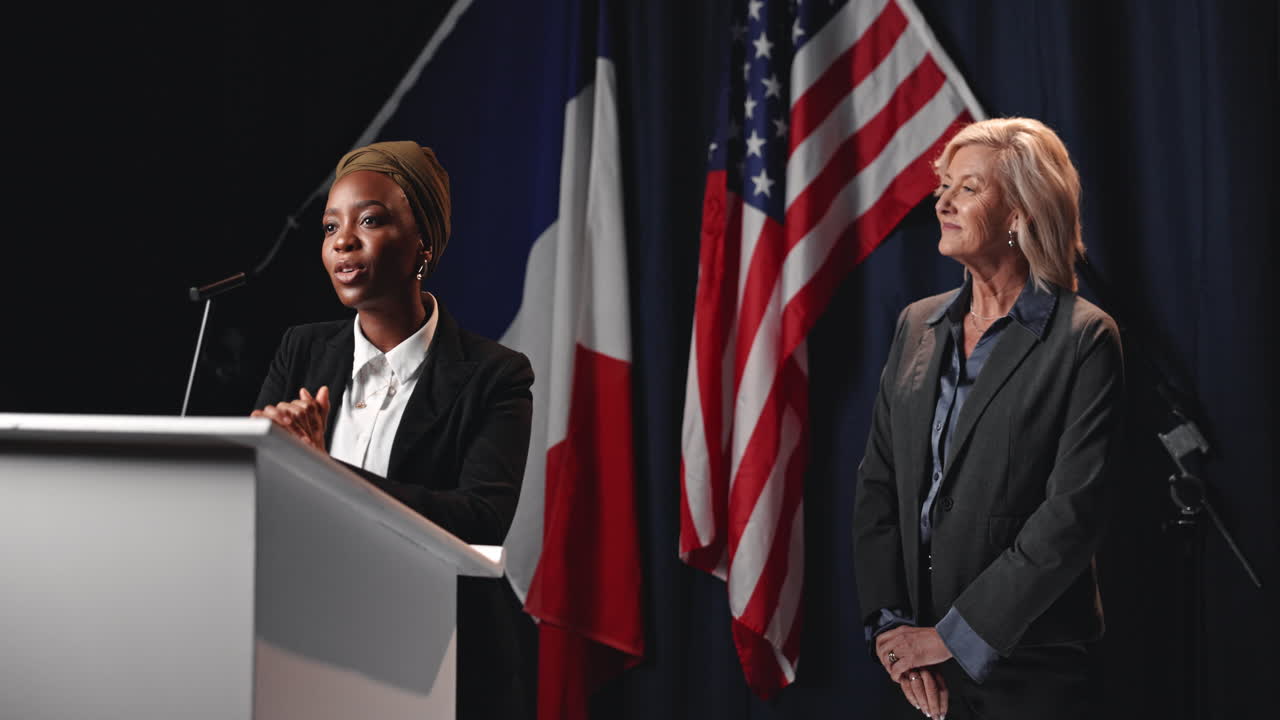 Women shaking hands in front of flags