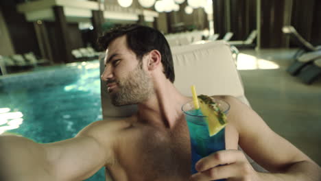 close up of man drinking cocktail by pool at hotel . happy man recording video