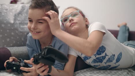 los hermanos disfrutan de los videojuegos en casa. la niña cierra los ojos al niño. los niños se divierten juntos.