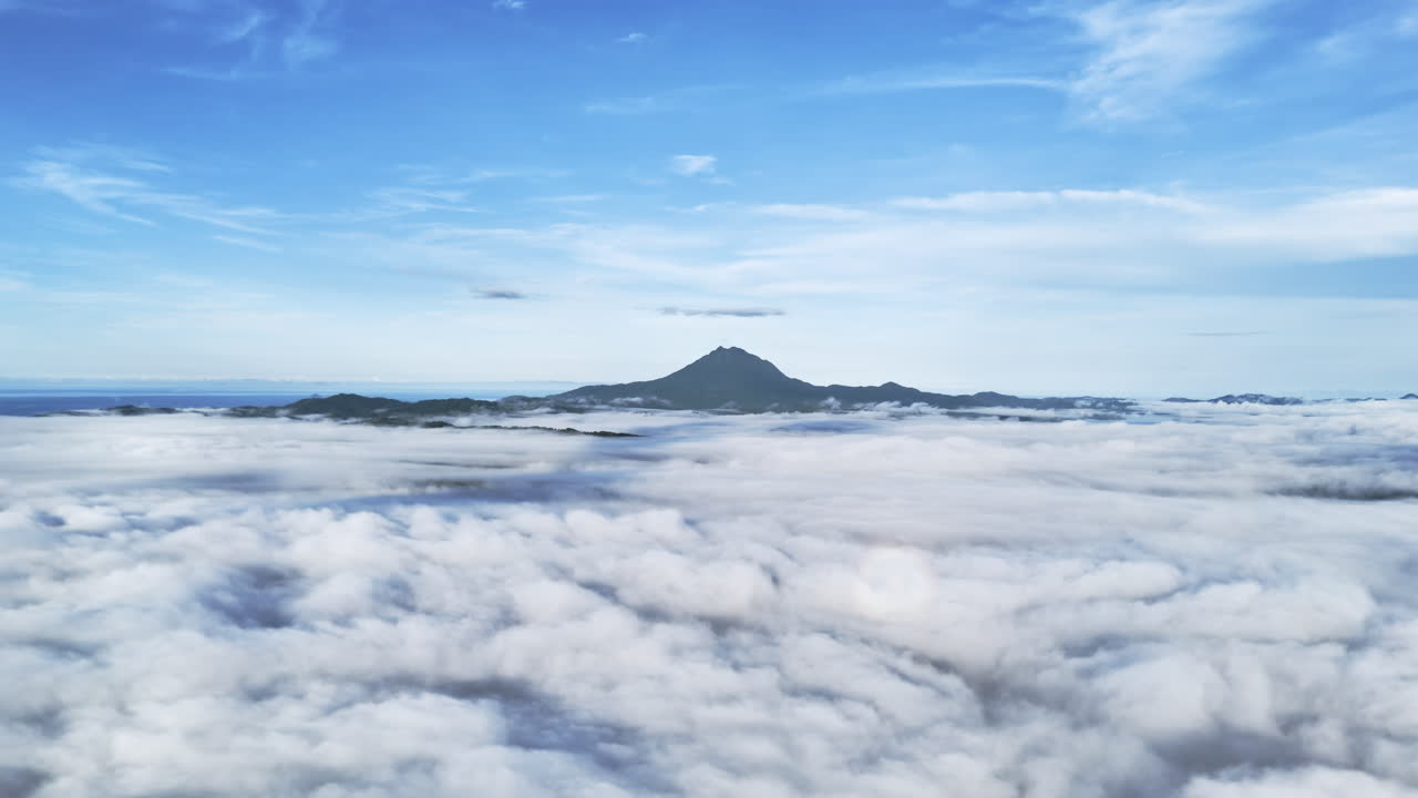 High-altitude aerial panning shot above Malampaya Sound during a foggy morning, featuring clouds below, Mount Capoas on the horizon, and a vivid blue sky