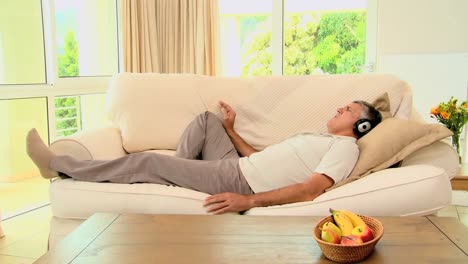 Man-lying-on-sofa-enjoying-music-with-headphones